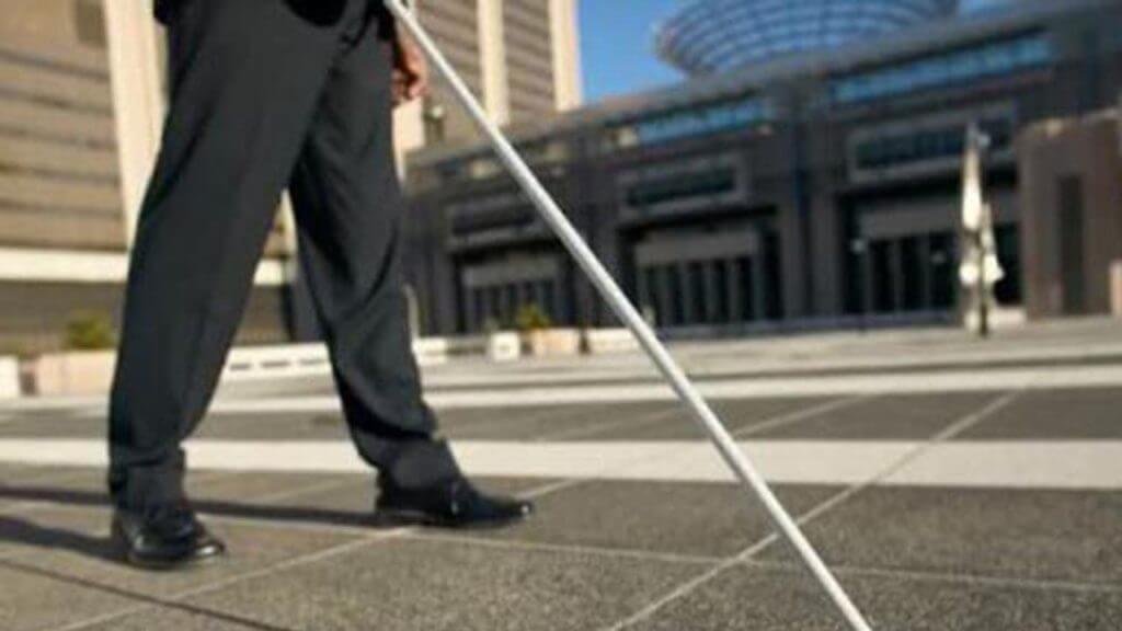 Fotografia delle gambe di una persona cieca con un bastone per orientarsi nella piazza di una città.